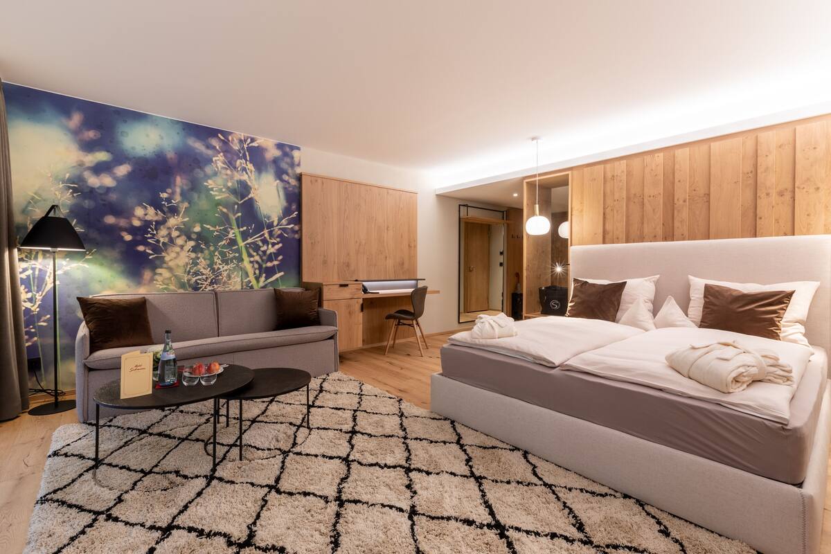 Ein modernes Hotelzimmer mit einem großen Bett, einer Couch, einem Schreibtisch und einem großen floralen Kunstwerk an der Wand.