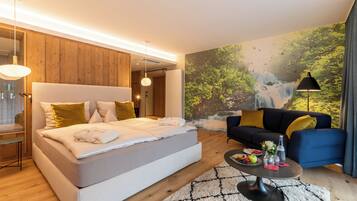 A modern hotel room with a large bed, a sofa, a coffee table, and a mural of a waterfall.
