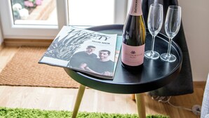 A room with a table holding a bottle of wine and two glasses, a magazine, and a view of a garden through a window. - Boutique Apartments Vienna (Vienna)
