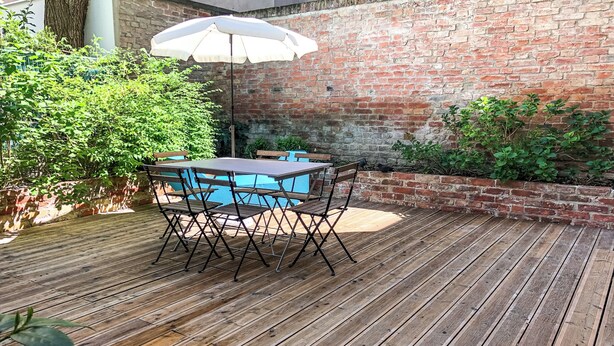 A wooden deck with a table and chairs, a white umbrella, and a brick wall. - Boutique Apartments Vienna (Vienna)