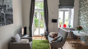 A living room with a grey sofa, a small table with a bottle and glasses, a TV, and a large window with curtains. - Boutique Apartments Vienna (Vienna)