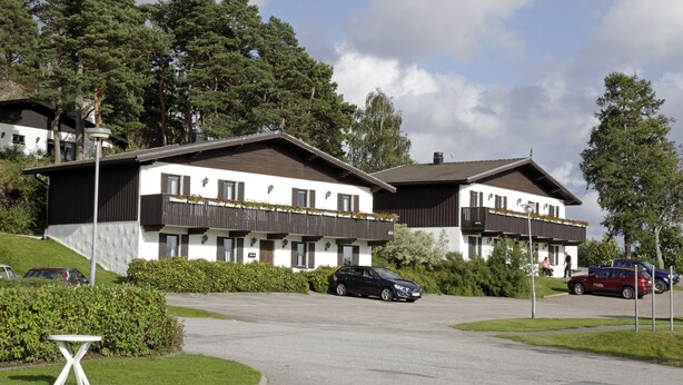 Ein zweistöckiges Gebäude mit Balkon, Parkplatz und einem kleinen Tisch.
