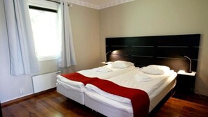 Ein Doppelbett mit roter Decke, ein Nachttisch mit Lampe und ein Fenster mit Vorhängen.