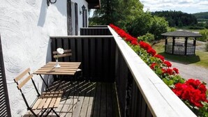 Eine Holzterrasse mit Tisch und Stühlen, eine weiße Wand mit Fensterläden und ein Garten mit roten Blumen.