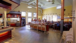 Ein großzügiges Restaurant mit hohen Decken, freiliegenden Leitungen und verschiedenen Sitzbereichen, darunter eine Bar und Esstische.