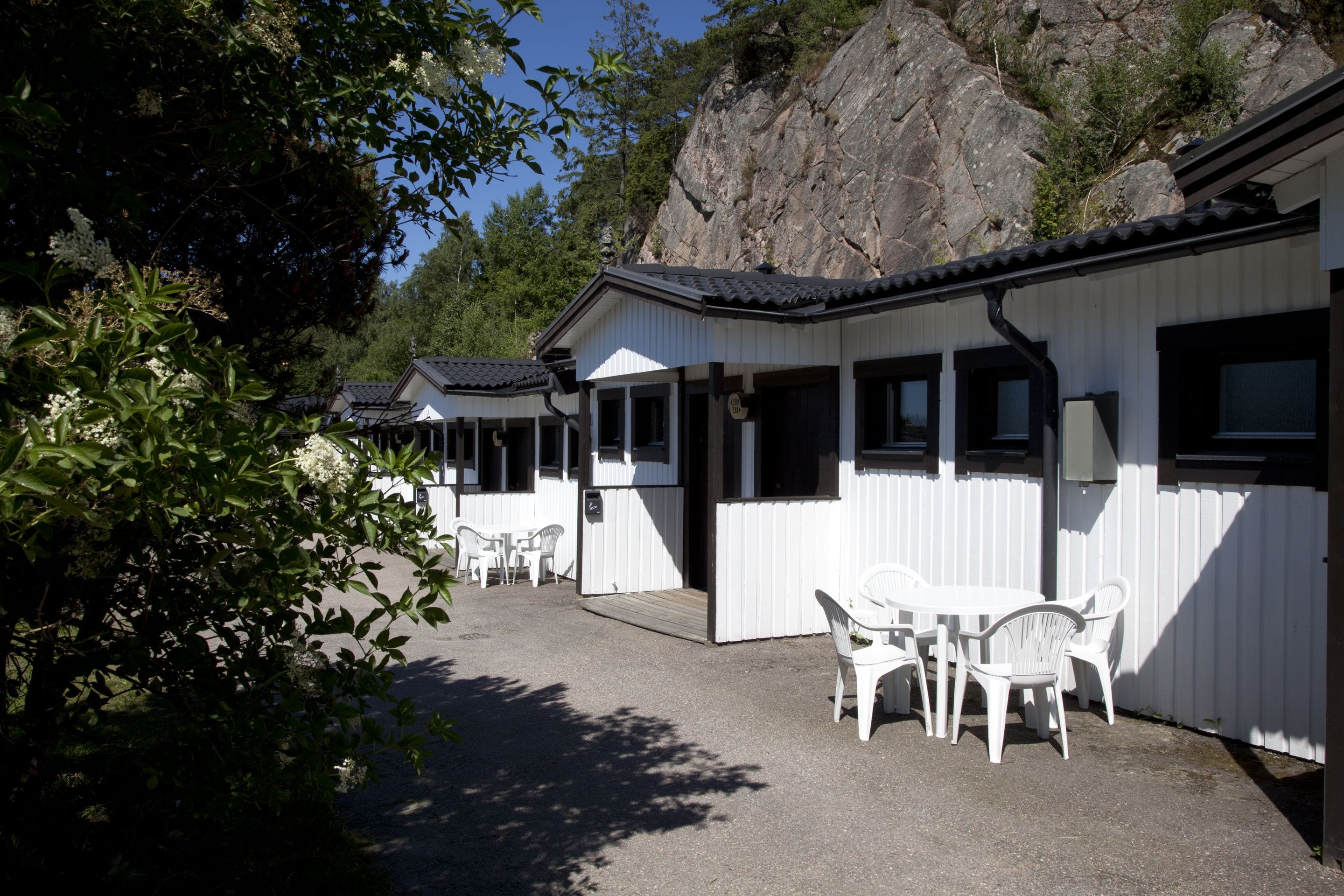 Une rangée de cabanes blanches aux bordures noires, chacune dotée d’un petit porche et d’une seule fenêtre.