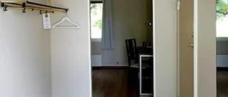 Um corredor com piso de madeira, um cabide e uma porta que dá para uma sala de jantar.