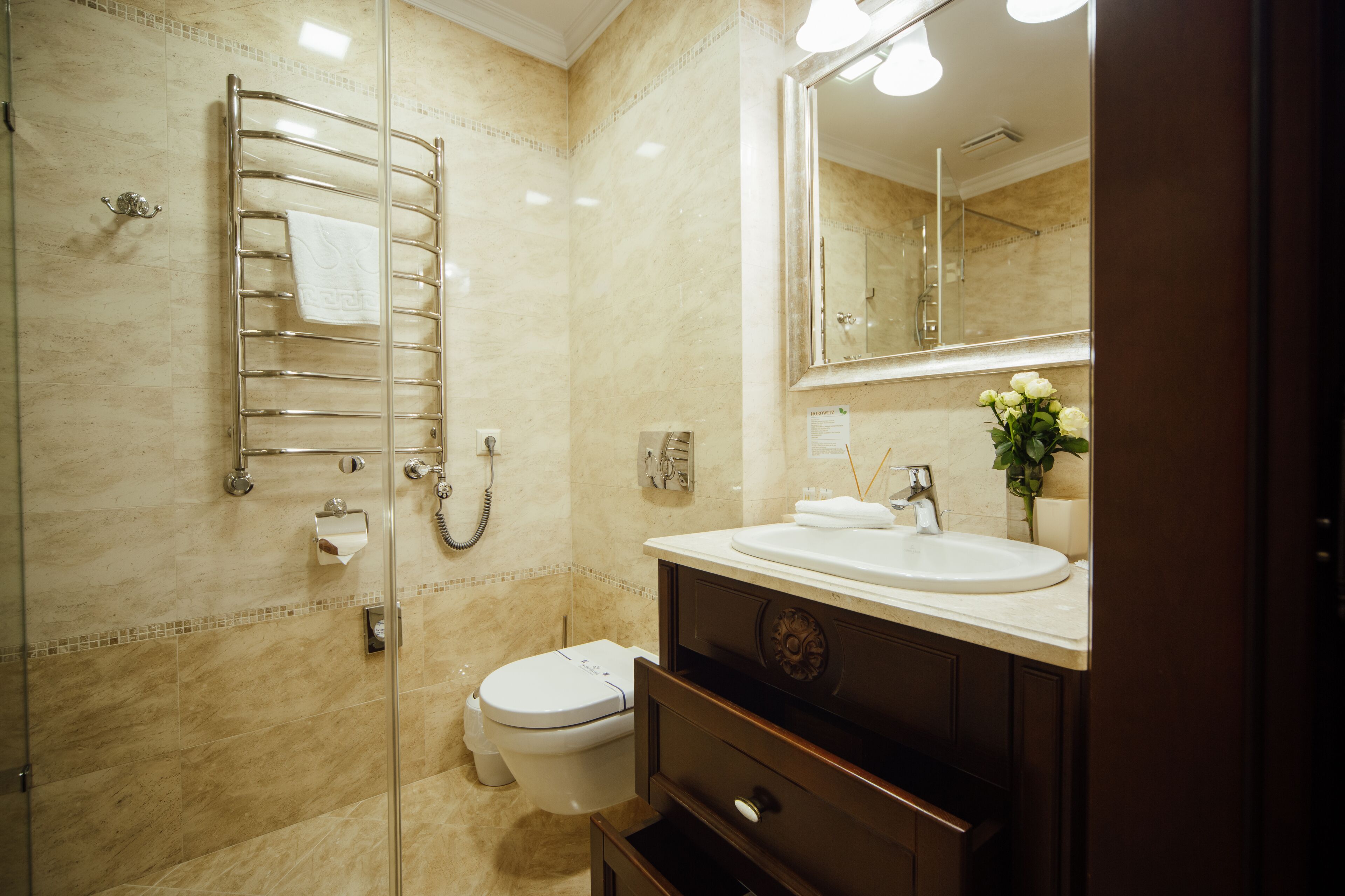 A bathroom with a glass shower enclosure, a toilet, a sink with a mirror, and a towel rack.