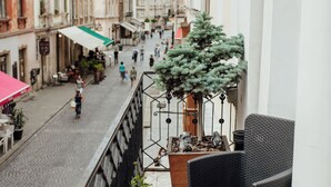 A balcony with a wicker chair, potted plants, and a cobblestone street below. - Apart-hotel Horowitz (Lviv)