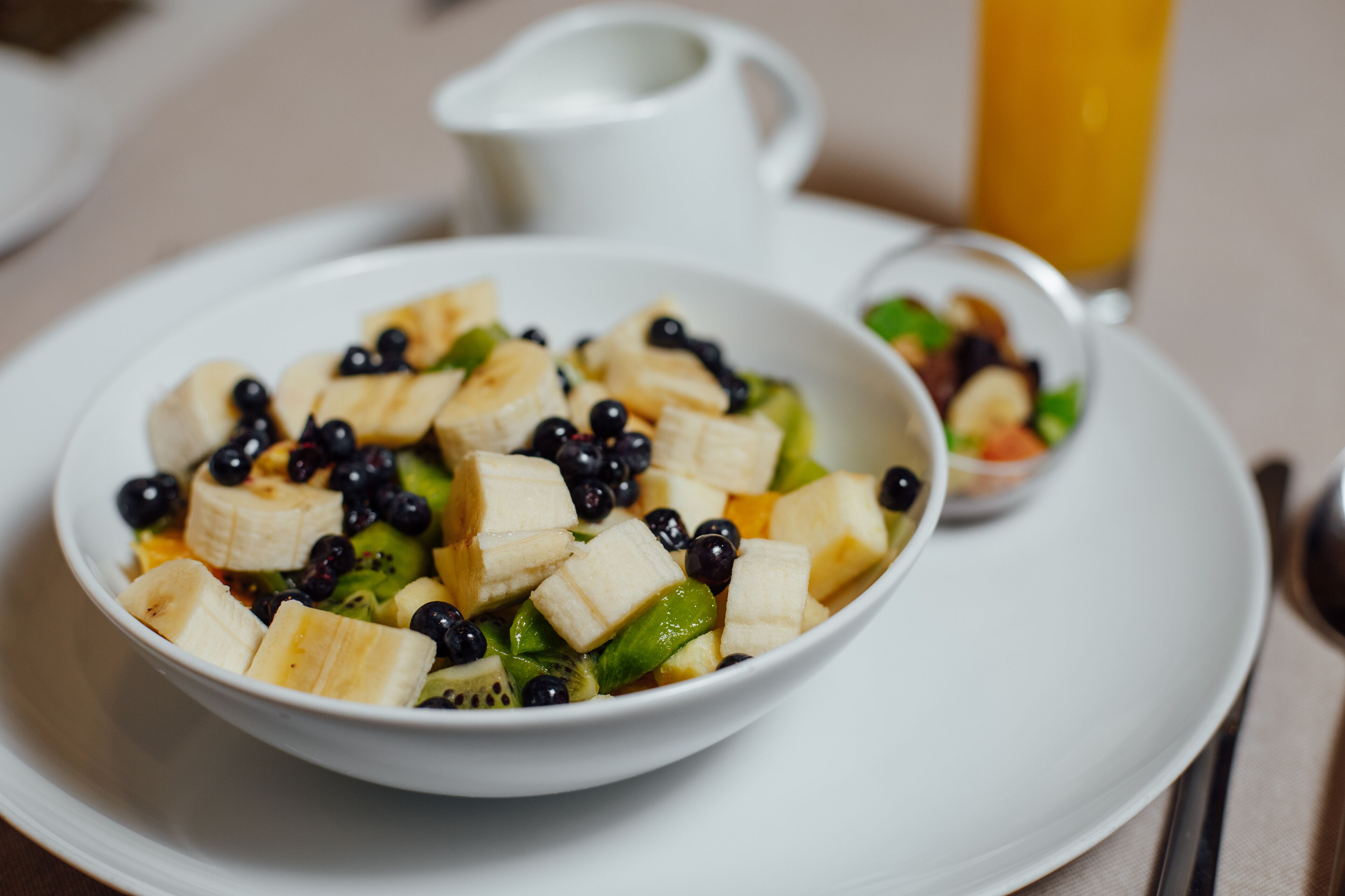 Un tazón de ensalada de frutas con plátanos, arándanos y kiwi sobre un plato blanco.