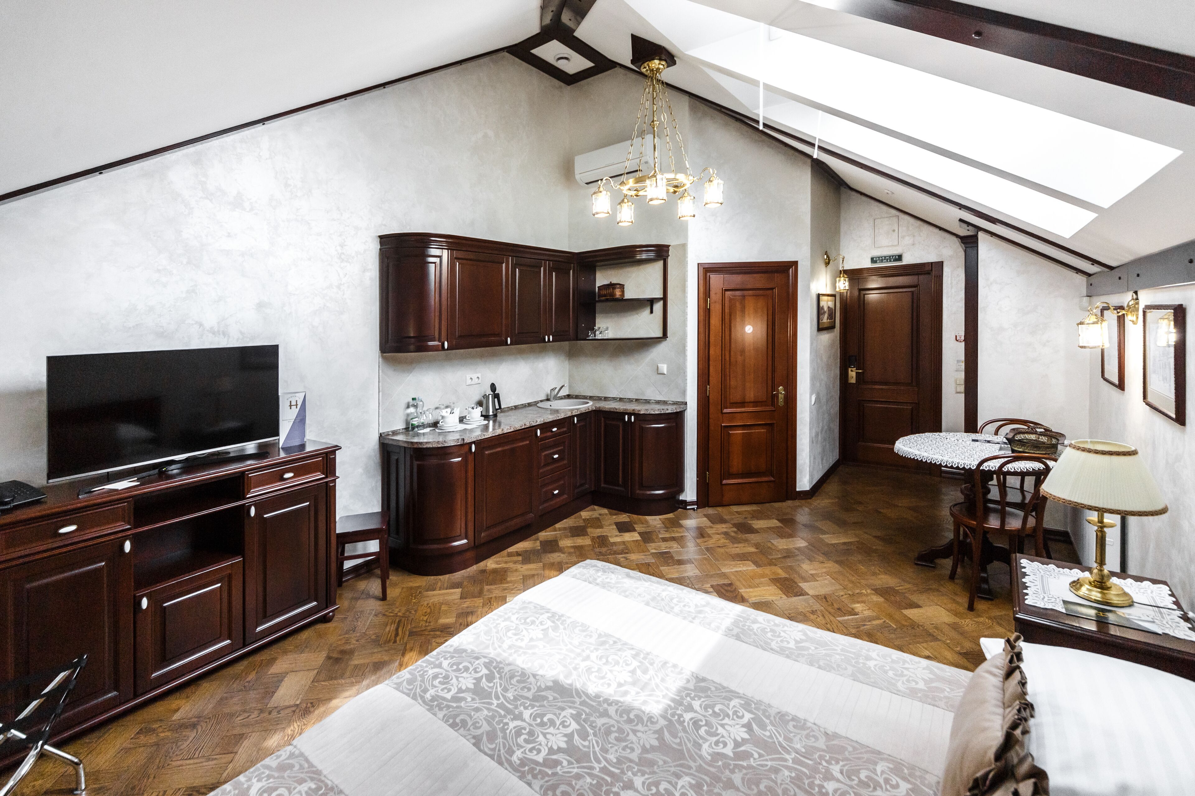 Cocina compacta con armarios de madera oscura, televisor integrado y candelabro.