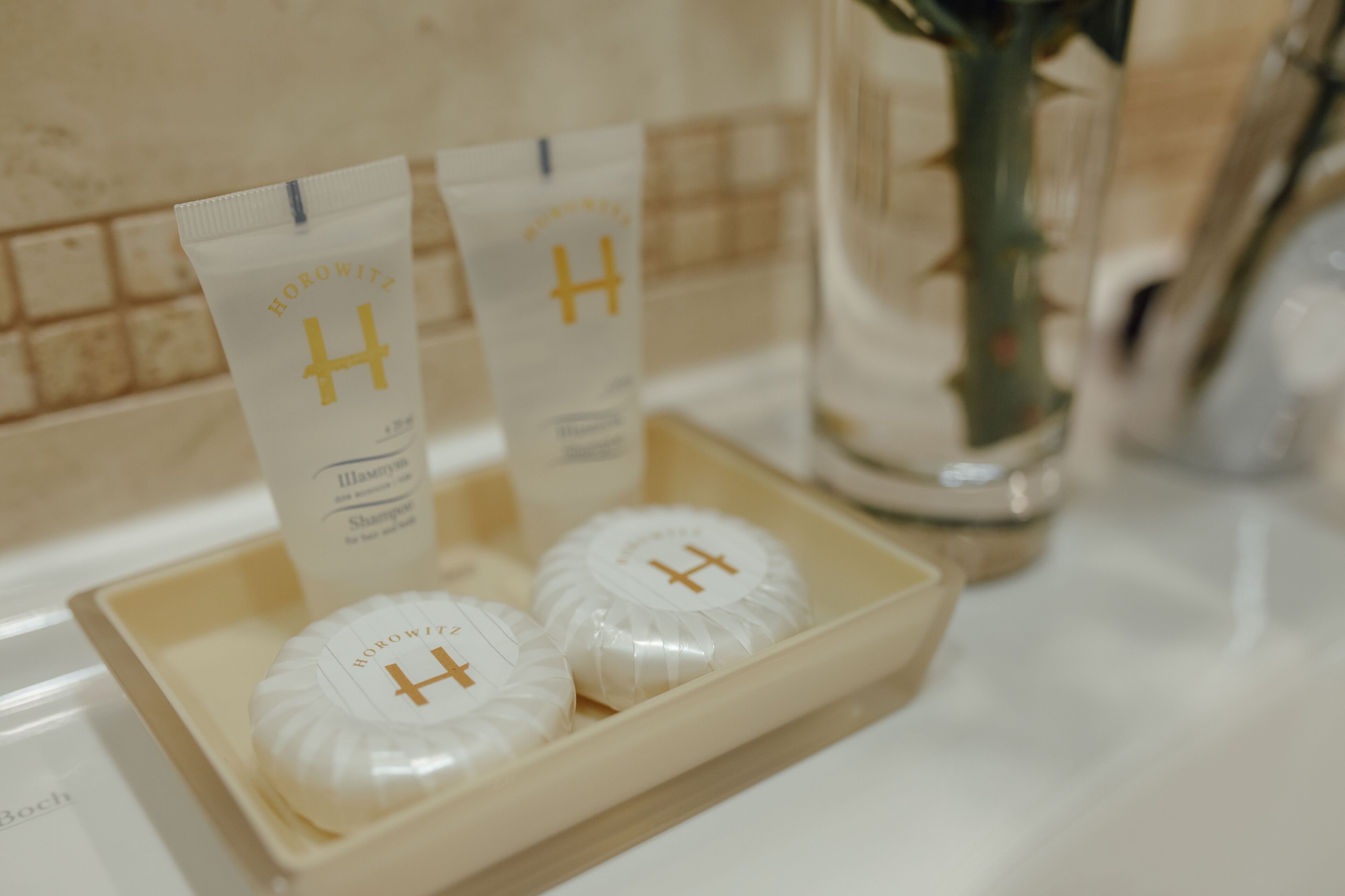 Una bandeja con dos jabones blancos y dos paquetes blancos con un logotipo dorado de 'H'.