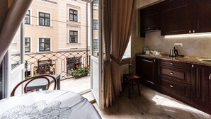 A compact kitchen with dark wooden cabinets, a countertop with a sink, and a window overlooking a street with a building and a shop. - Apart-hotel Horowitz (Lviv)