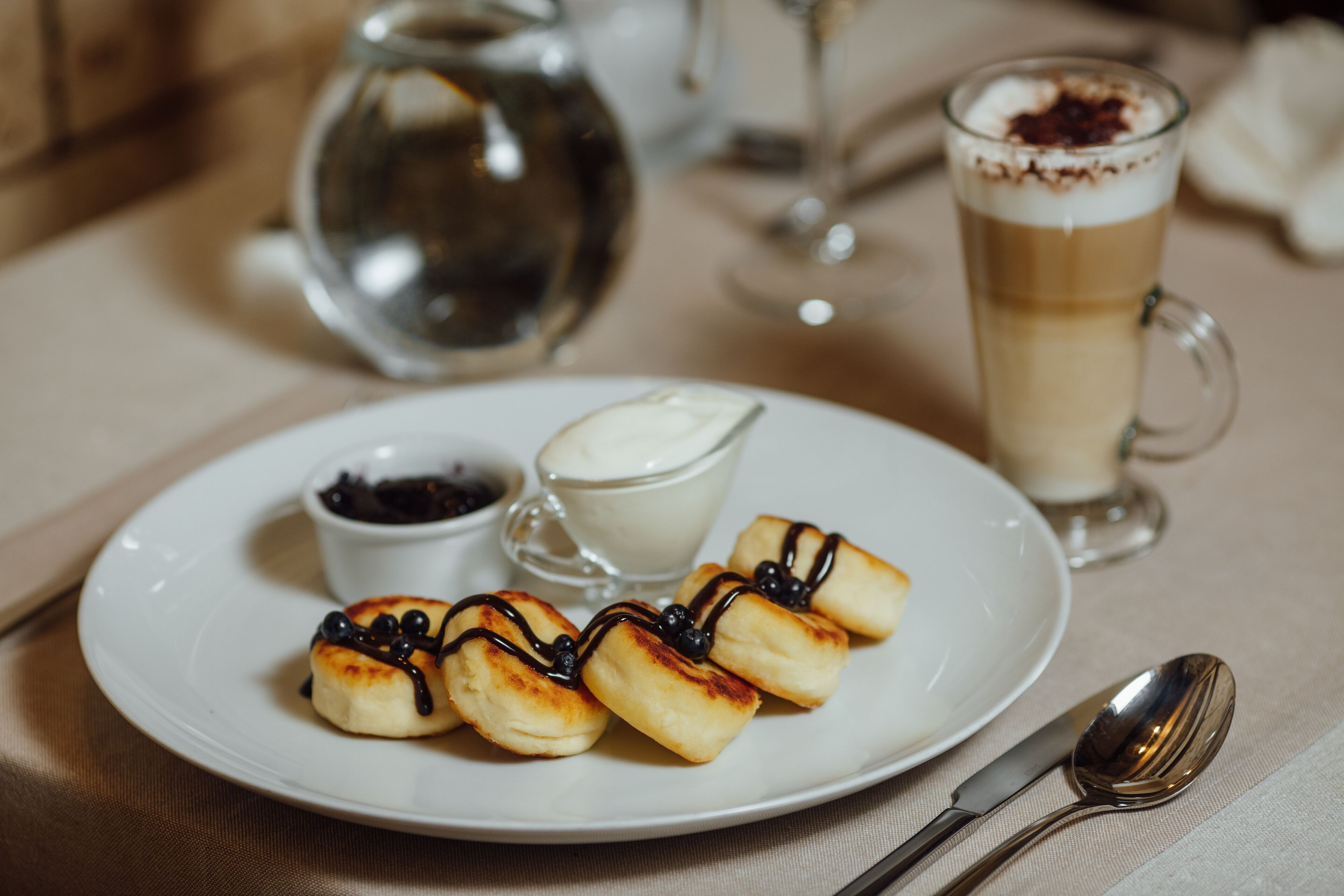 A plate with dessert items, a cup of coffee, and a small bowl of cream.