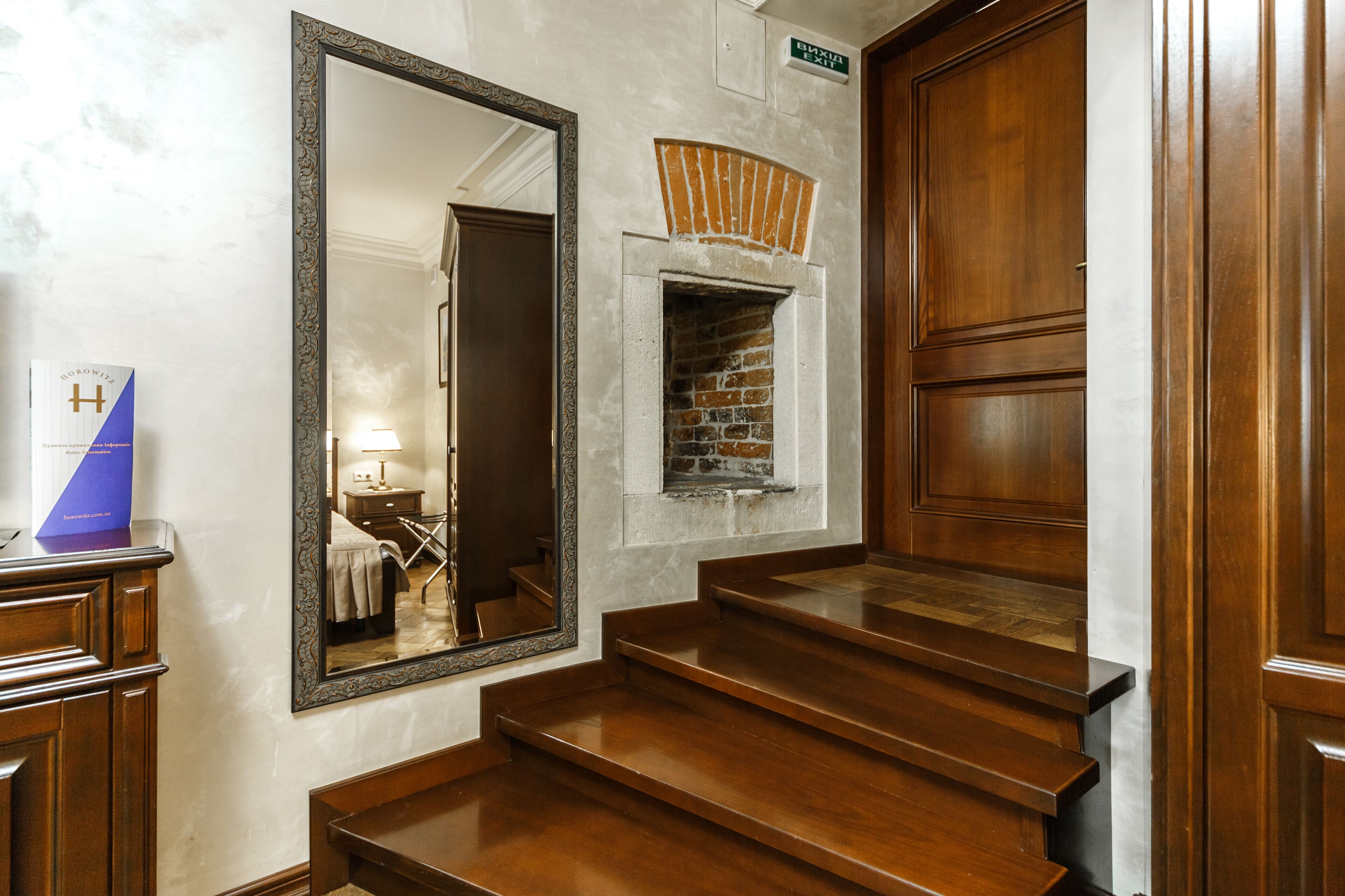 A staircase with wooden steps leading to a door, a large mirror on the wall, and a small brick fireplace.