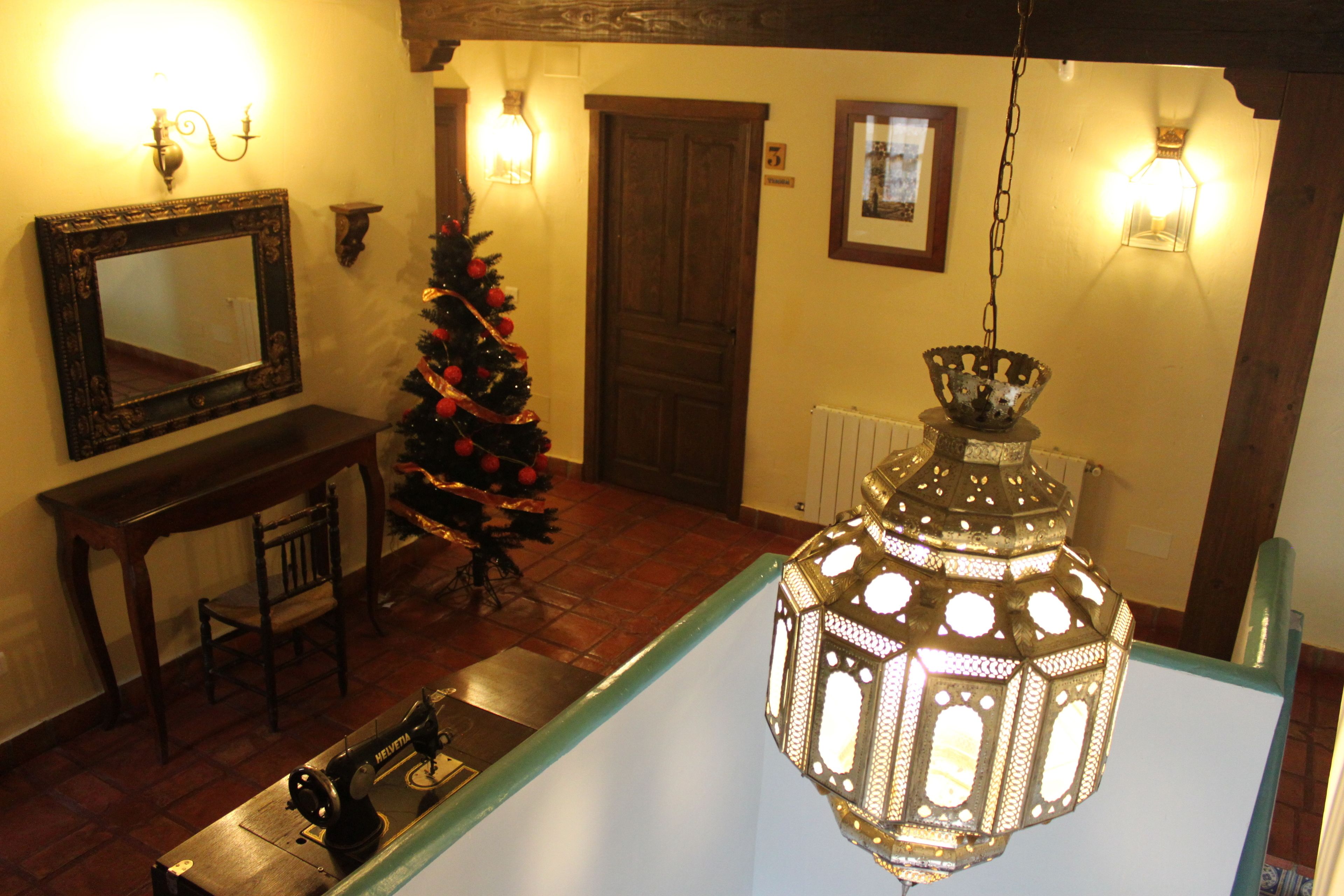 A room with a wooden floor, a Christmas tree, a sewing machine, and a hanging lantern.