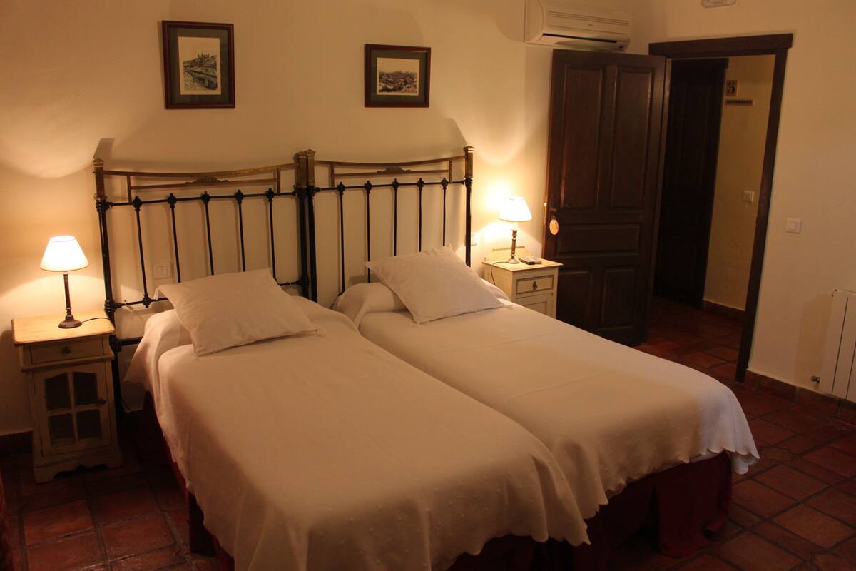 Een kamer met twee eenpersoonsbedden, een nachtkastje met een lamp, een houten deur en een radiator aan de muur.