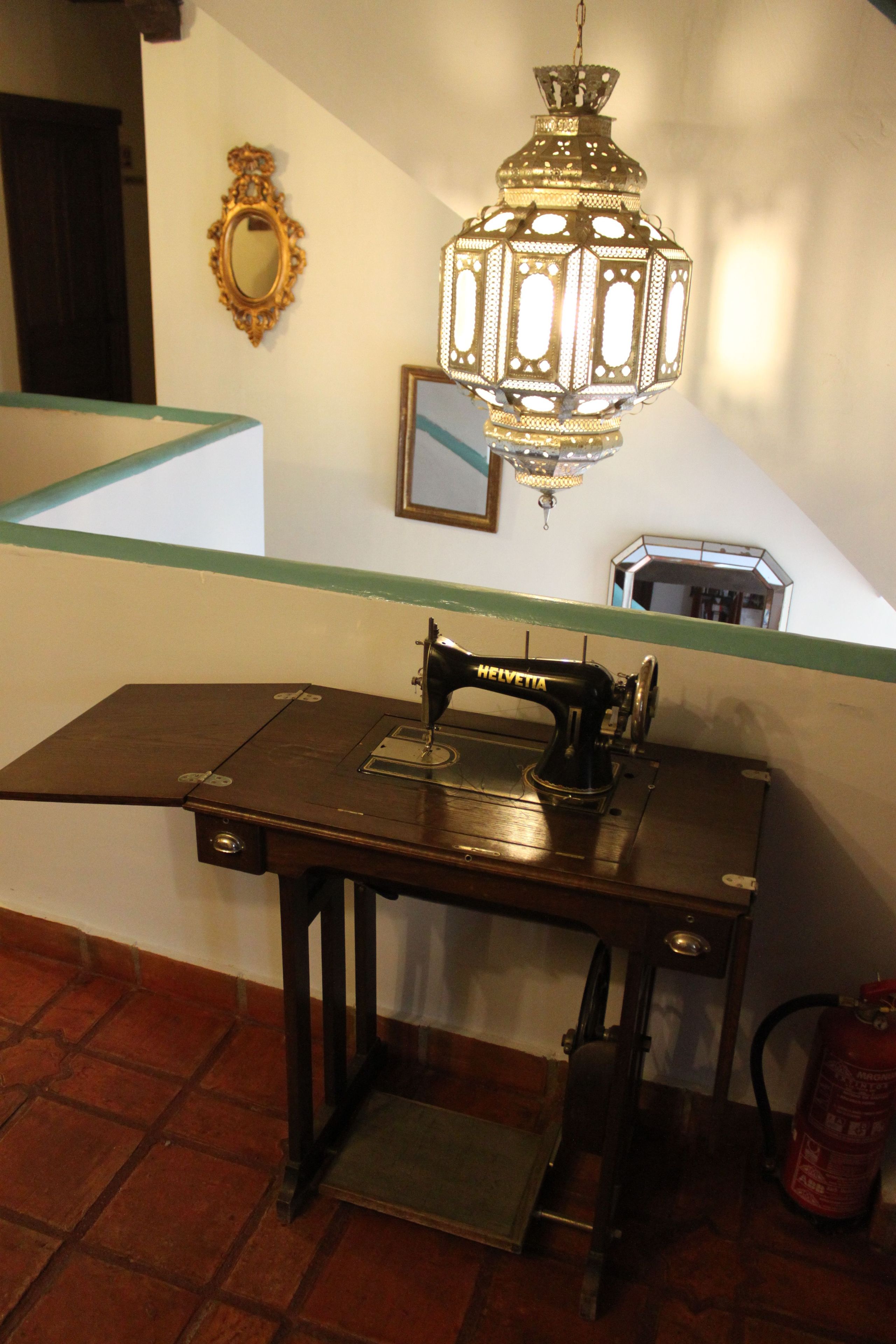 Una máquina de coser sobre una mesa de madera, con un espejo y un farol en la pared.
