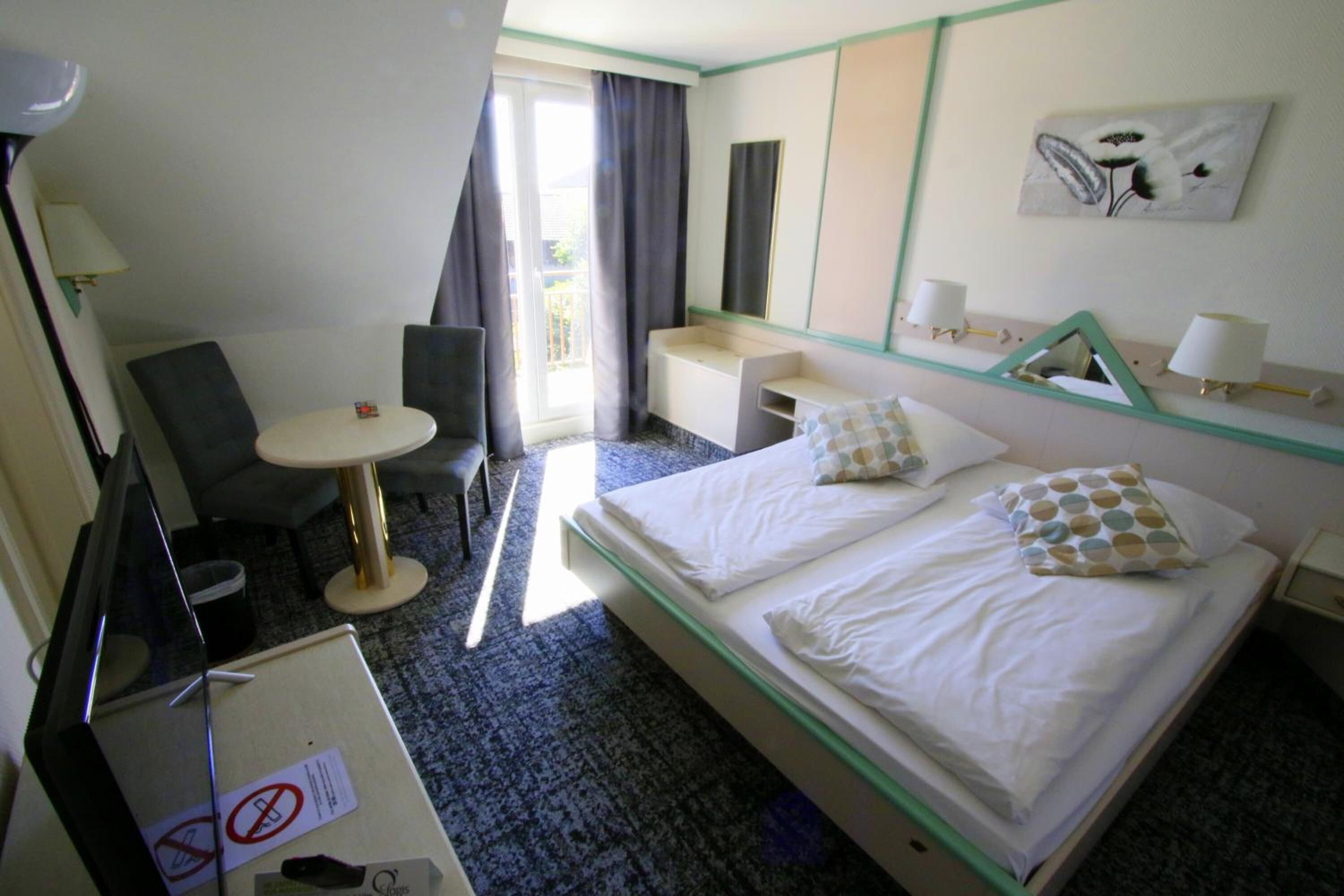 Ein Hotelzimmer mit Bett, Schreibtisch, Stuhl, kleinem Tisch und einem Fenster mit Vorhängen.