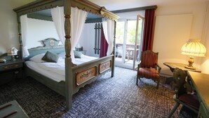 A four-poster bed with a canopy, a wooden nightstand with a lamp, a chair, and a table with a lamp. - Hôtel les Portes de la Vallée (Turckheim)