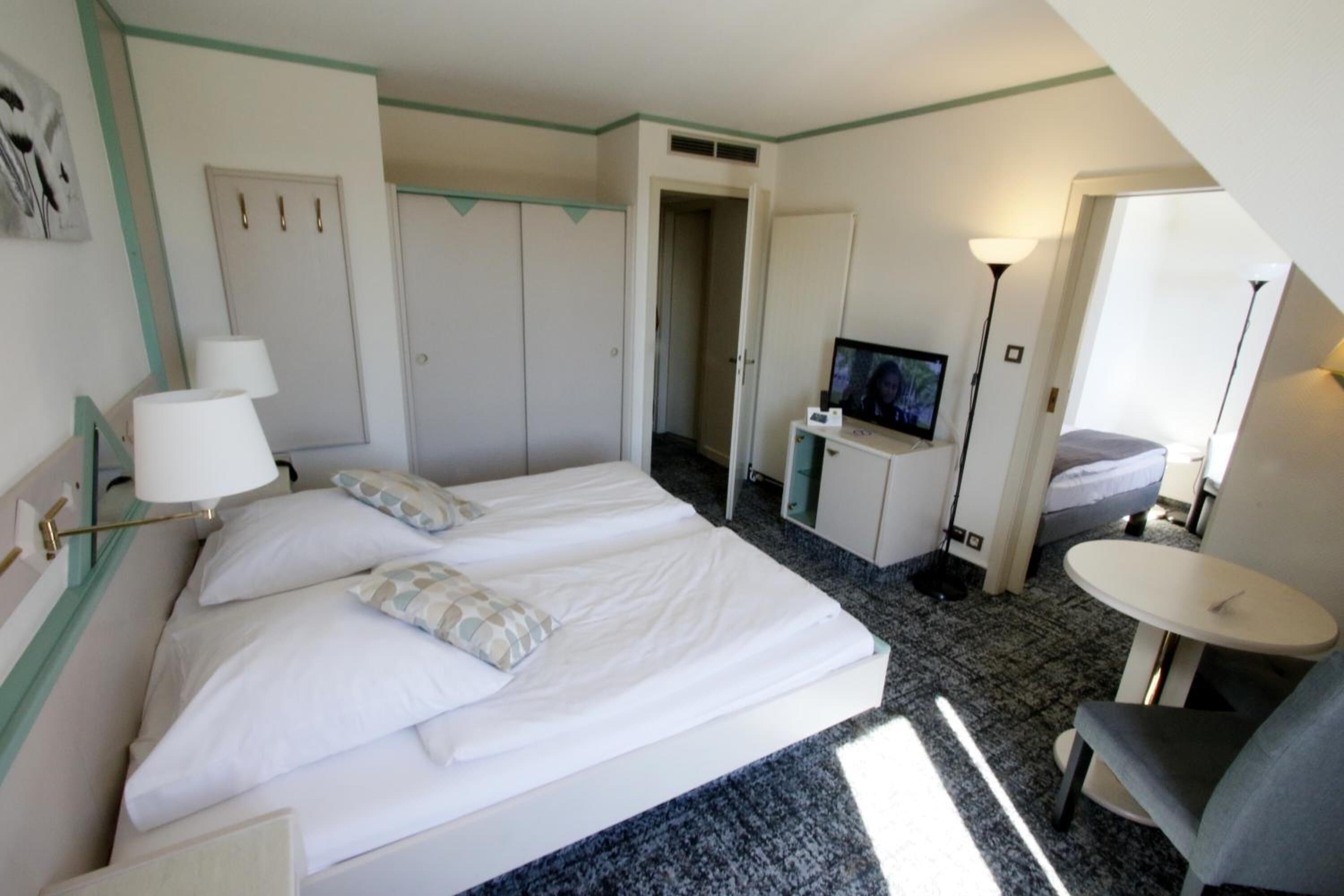 A hotel room with a double bed, a desk with a television, a chair, and a small table.