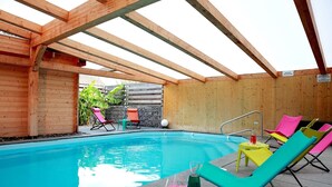 An indoor swimming pool with wooden beams, colorful lounge chairs, and a small table with glasses and a bottle. - Hôtel les Portes de la Vallée (Turckheim)