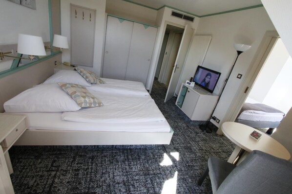 A hotel room with two beds, a desk, a chair, a TV, and a small table. - Hôtel les Portes de la Vallée (Turckheim)