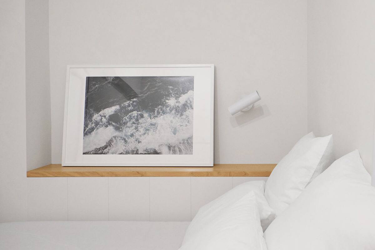 A white bathroom with a framed photograph on the wall, a toilet paper holder, and a white sink.
