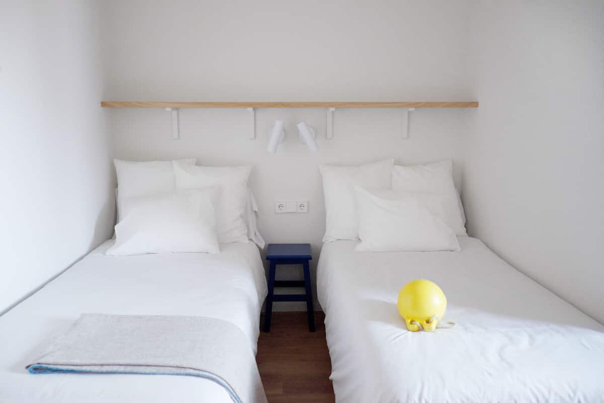 A twin room with two beds, a small table, and a shelf above the beds.