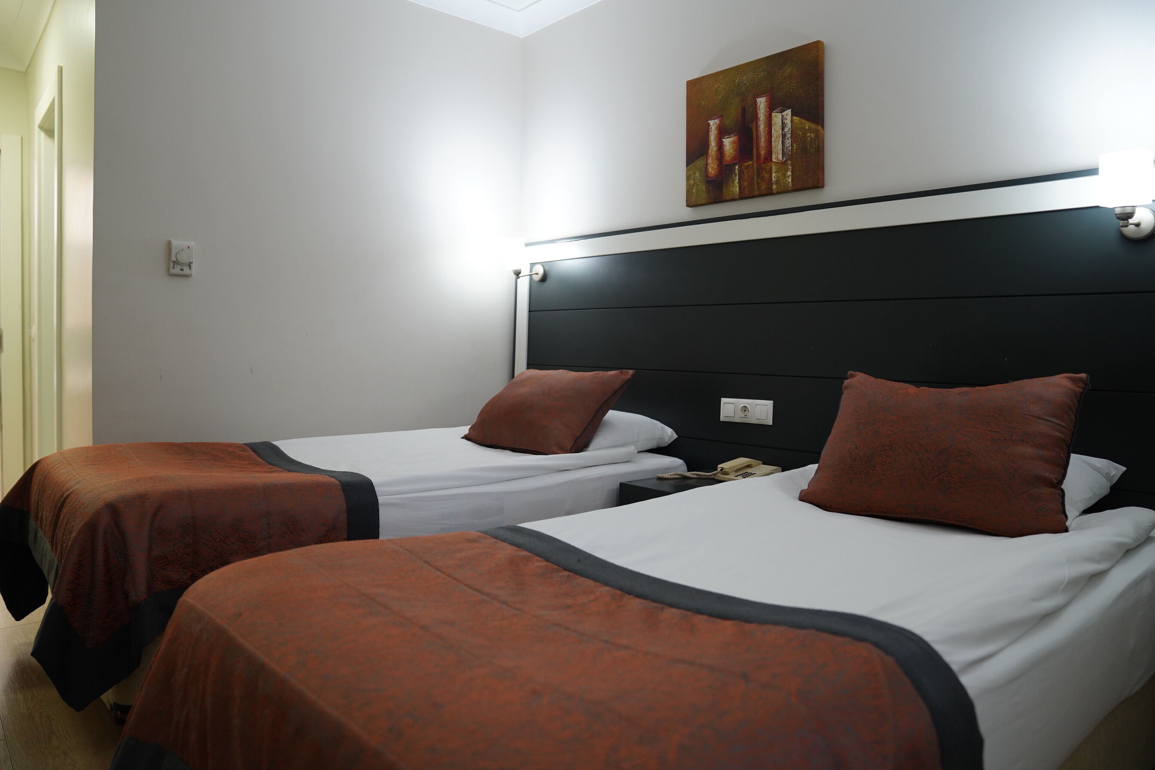 A hotel room with two single beds, each with a brown bedspread and pillow, a black headboard, and a painting on the wall.