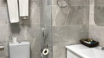 A modern bathroom with a toilet, bidet, and a sink with a basket of toiletries.