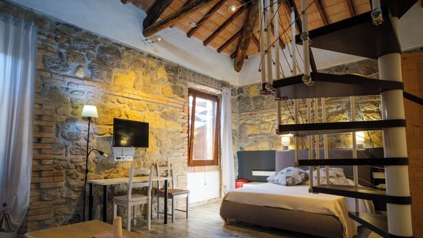 A bedroom with a stone wall, a bed, a desk with a chair, a TV, and a staircase. - Locanda Villa Naumanni  (Tarquinia)