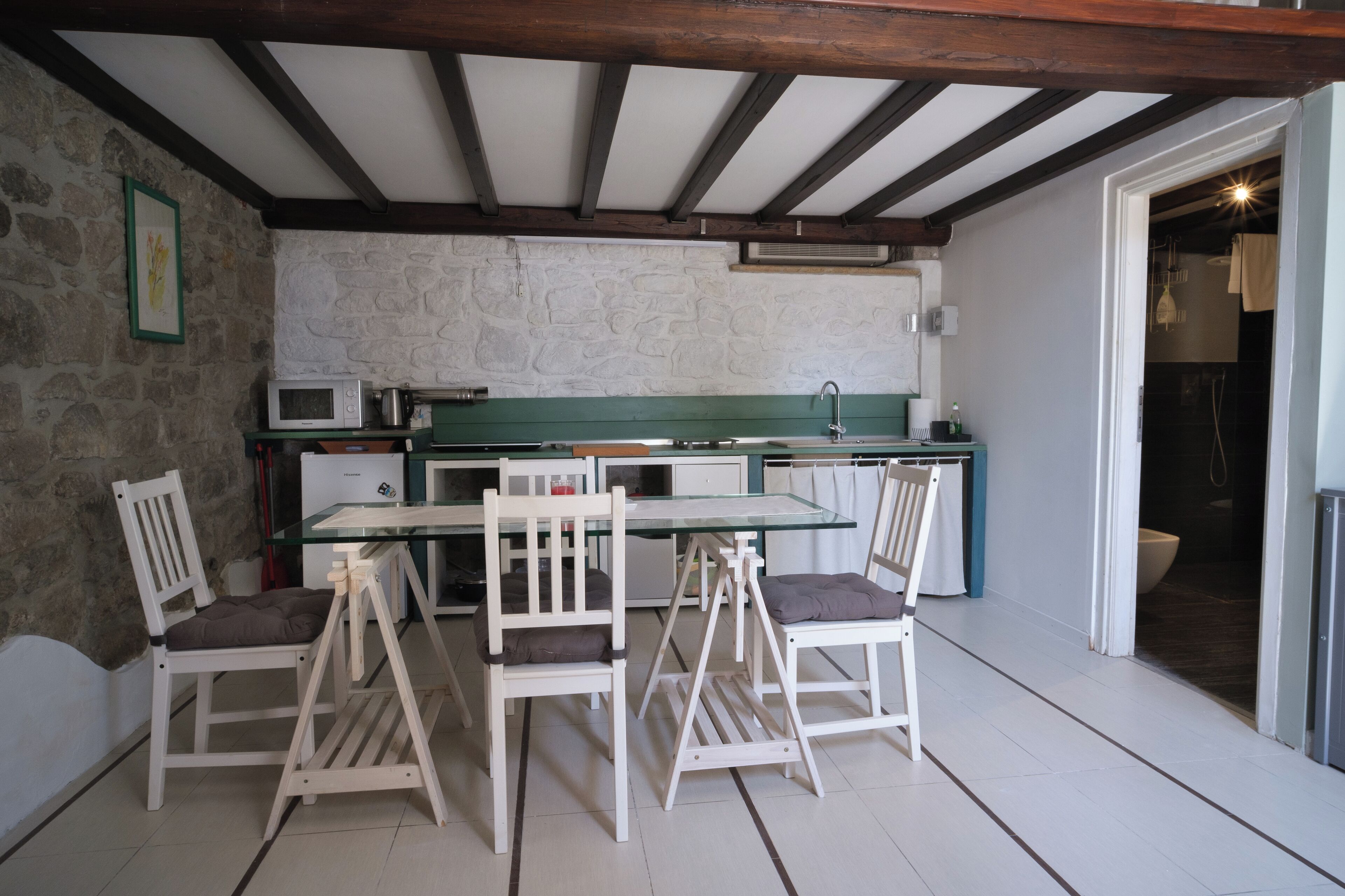 A kitchen with a stone wall, a microwave, a sink, and a dining area with chairs and a table.