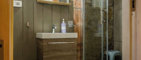 A bathroom with a wooden vanity, a glass shower enclosure, and a small stool.