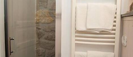 A bathroom with a stone wall, a glass shower door, a white sink, and a towel rack.