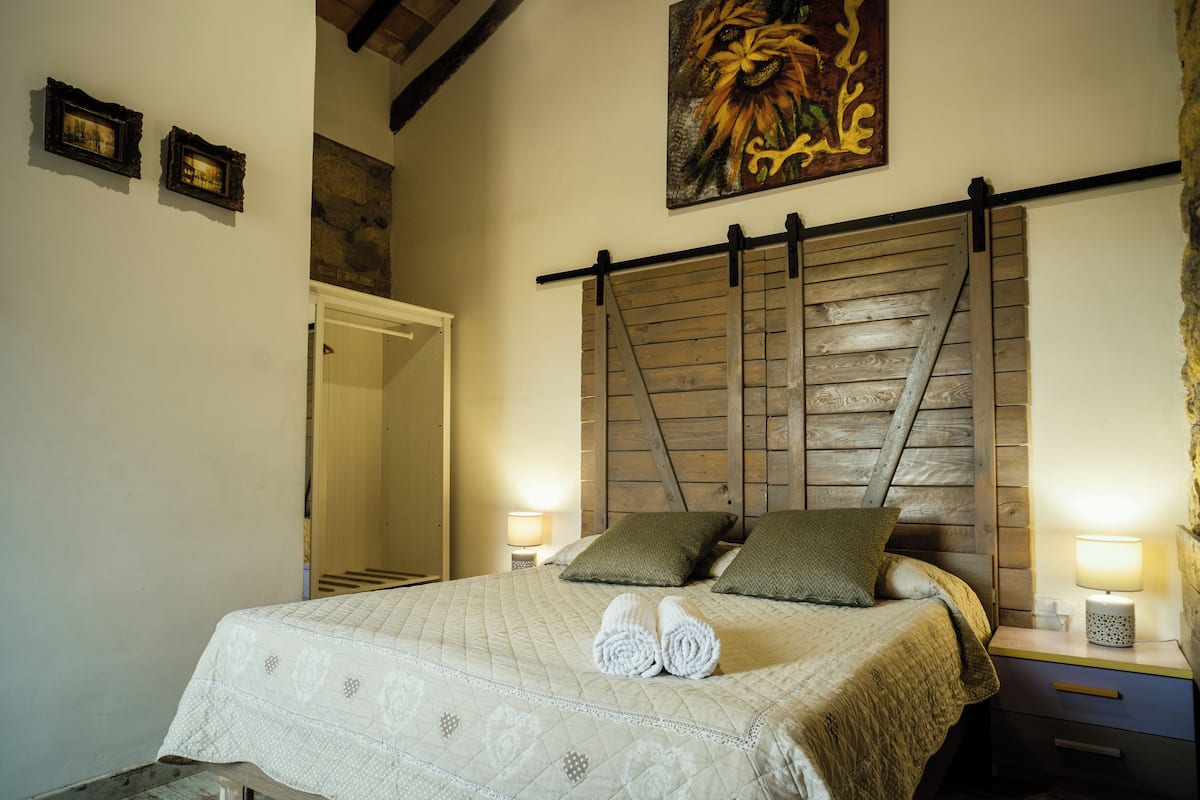 Ein Schlafzimmer mit einem hölzernen Kopfteil, einem Bett mit einer gesteppten Bettdecke, zwei Kissen und einem Nachttisch mit einer Lampe.