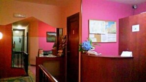 A reception area with a wooden desk, a blue flower vase, and a bulletin board on a pink wall. - Hotel Solpor (Vigo)