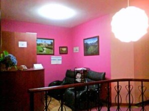 Una habitación con paredes rosas, un mostrador de recepción de madera, un sofá negro y una escalera con barandilla metálica.