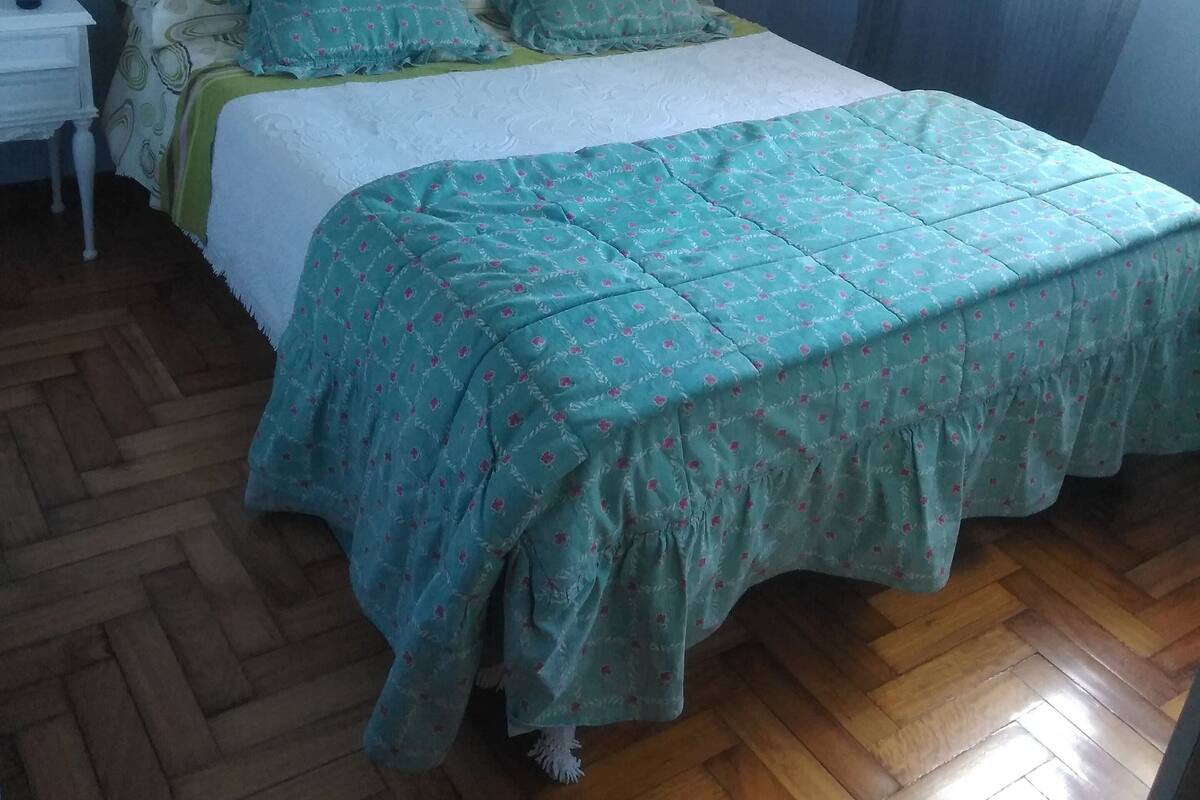 A bedroom with a bed, a nightstand, and a wooden floor.