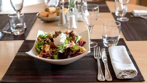Une table à manger élégamment dressée, avec une salade, des verres à vin et des couverts.
