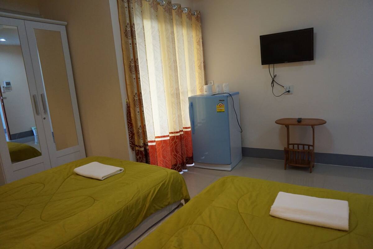 Habitación de hotel con dos camas, un televisor, un refrigerador y una mesita.