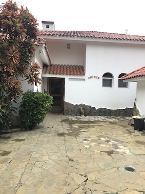 A white building with a tiled roof, a stone-paved courtyard, and a small garden area with a tree and shrubs. - Mariposa (Sosúa)