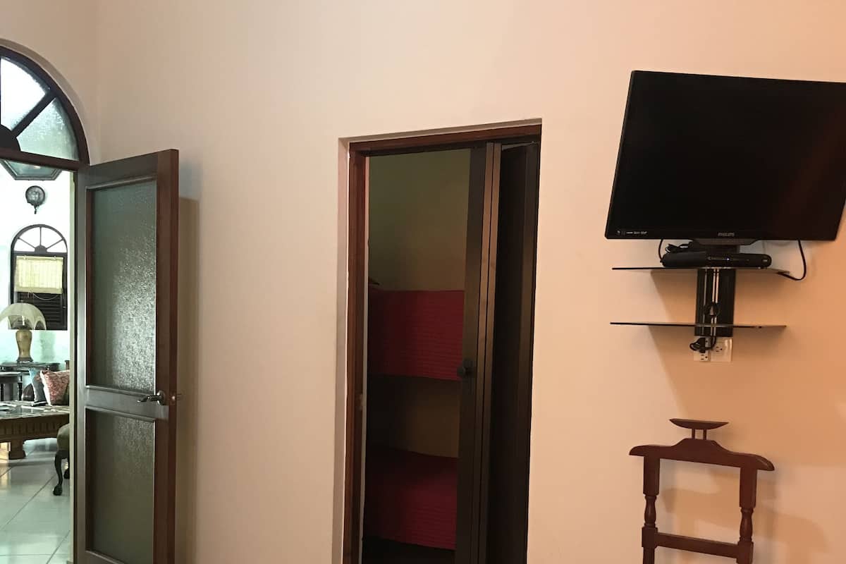 Une pièce dont le sol est carrelé, avec un téléviseur fixé au mur et une porte donnant sur une autre pièce.