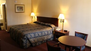 A hotel room with a large bed, two bedside lamps, a small table with a chair, and a framed picture on the wall. - Western Inn (Gonzales)