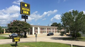 A Western Inn building with a clear sky, a parking lot, and a no trailer trucks sign. - Western Inn (Gonzales)