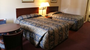 A hotel room with two beds, a wooden headboard, a round wooden table, and a chair. - Western Inn (Gonzales)