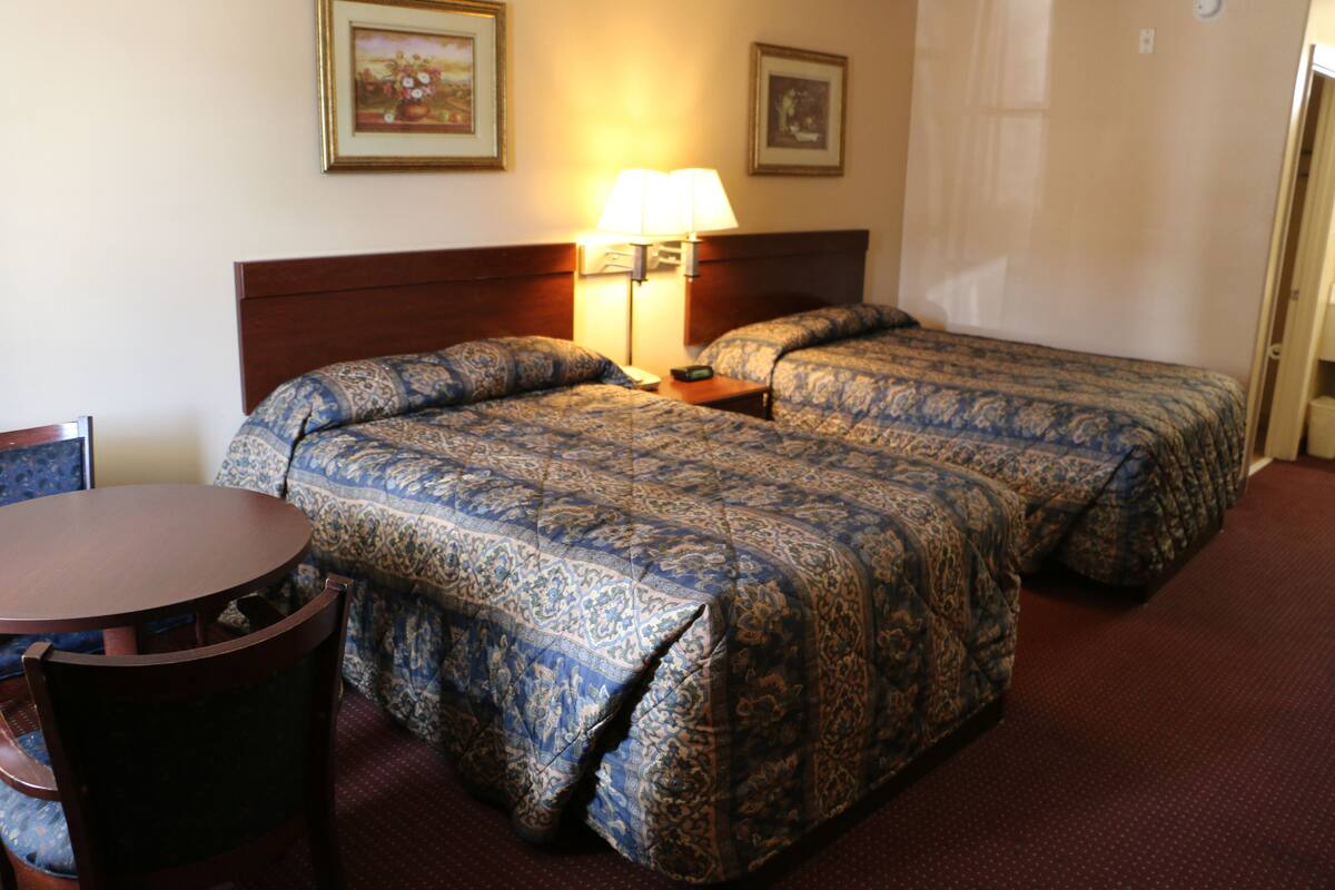 A hotel room with two beds, a wooden headboard, a round wooden table, and a chair.