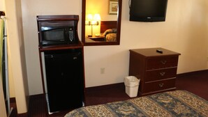 A hotel room with a microwave, a television, a dresser, and a trash can. - Western Inn (Gonzales)
