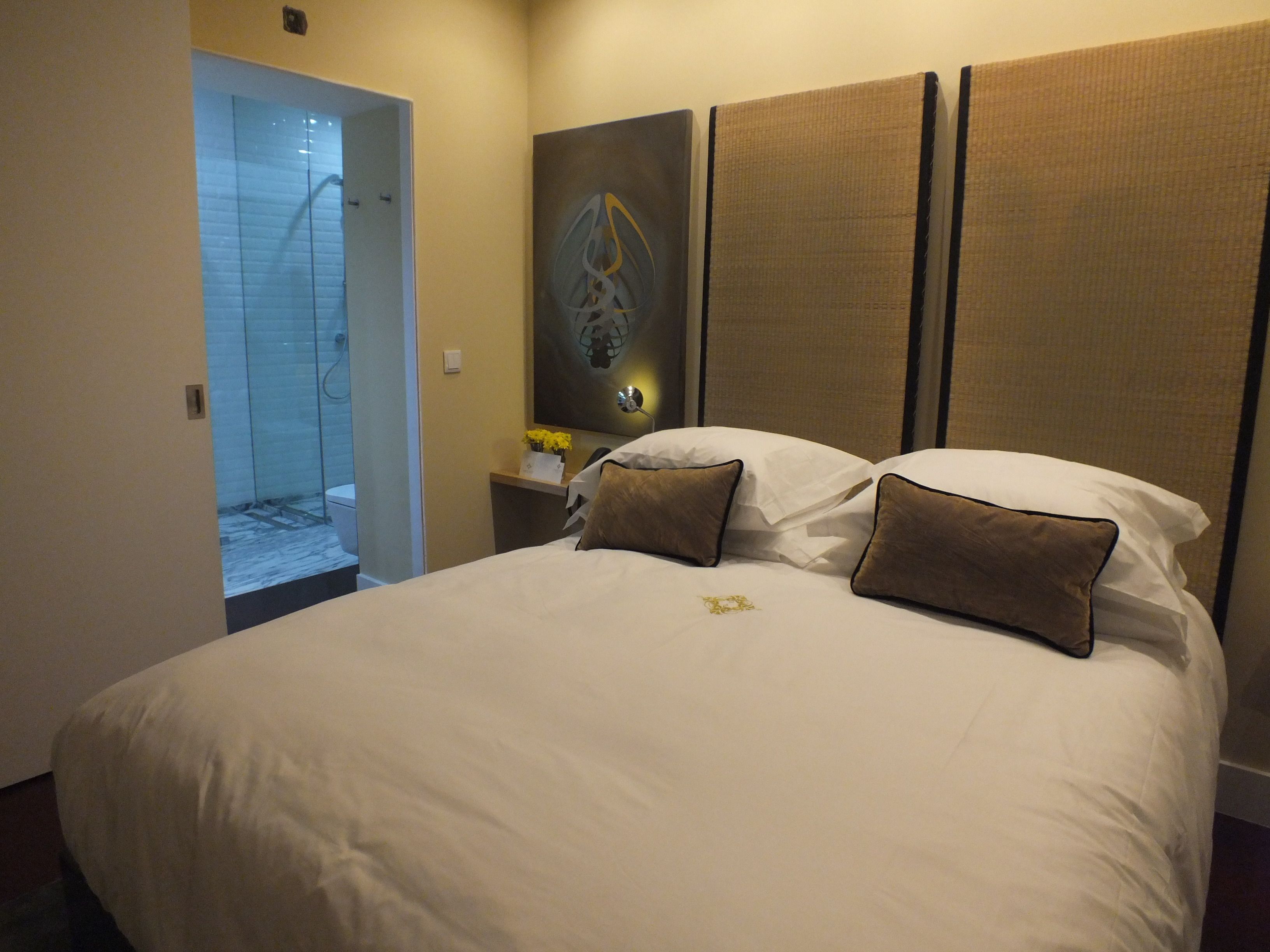 A hotel room with a large bed, a nightstand with a vase of flowers, and a painting on the wall.