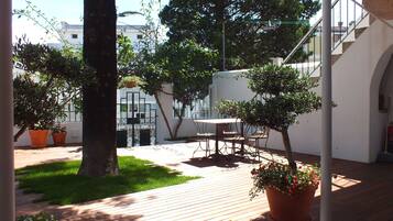 A wooden deck with a table and chairs, surrounded by potted plants and a grassy area.